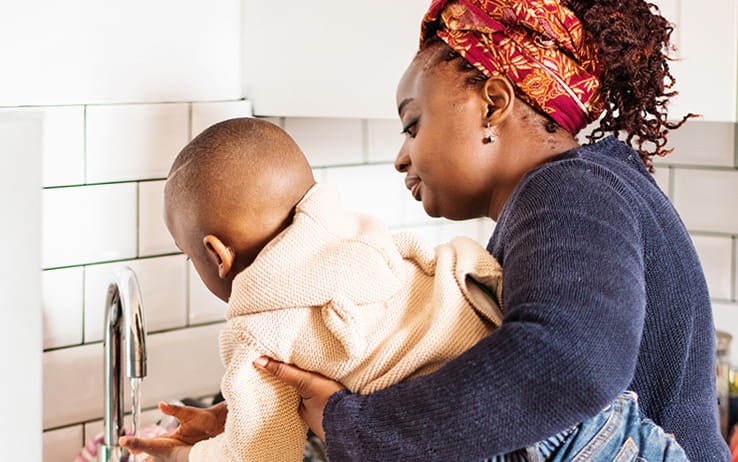 Woman holding child at a sink, washing hands