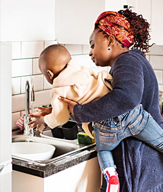 Woman holding child at a sink, washing hands
