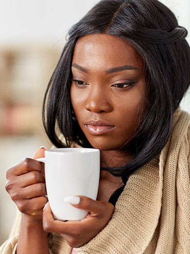 Sick woman wrapped in blanket, holding mug of tea